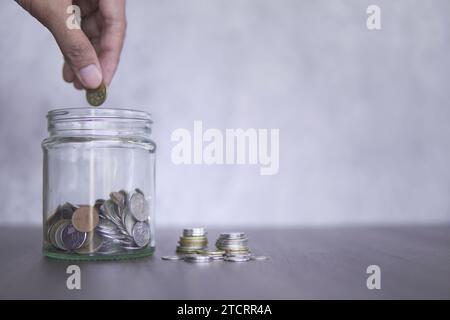Hand, die eine Münze in ein Glas voller Münzen steckt. Kopierbereich für Text. Geld sparen, Rentenplanungskonzept. Stockfoto