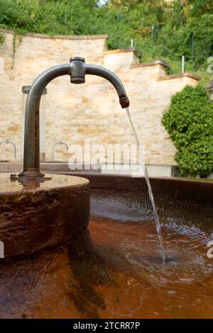 Trinkwasser strömt aus dem Wasserhahn auf der Straße. Ein alter rostiger Wasserhahn, aus dem Wasser in einen Wassertank fließt. Mineralische Trinkwasserquelle Stockfoto