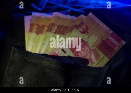 100 000 Rupiah in schwarzer Hosentasche, optisches Leuchtblau Stockfoto