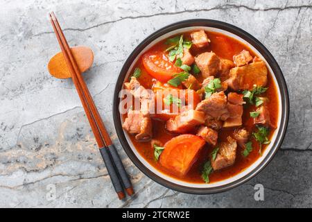 Indonesischer Schweinebauch mit Tomaten, Zwiebeln, süßer Sojasauce und asiatischen Gewürzen in einer Schüssel auf dem Tisch. Horizontale Draufsicht von oben Stockfoto