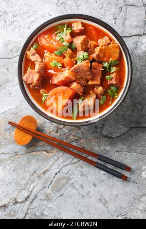 Asiatischer Schweinebauch, gedünstet mit Tomaten, süßer Sojasauce und Gewürzen in einer Schüssel auf dem Tisch. Vertikale Draufsicht von oben Stockfoto