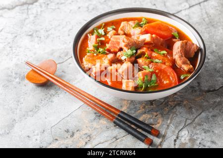 Indonesischer Schweinebauch mit Tomaten, Zwiebeln, süßer Sojasauce und asiatischen Gewürzen in einer Schüssel auf dem Tisch. Horizontal Stockfoto