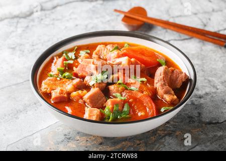 Scharfer Schweinebauch mit Tomaten, Zwiebeln, süßer Sojasauce und Gewürzen in einer Schüssel auf dem Tisch. Horizontal Stockfoto