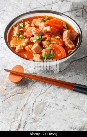 Asiatischer Schweinebauch, gedünstet mit Tomaten, süßer Sojasauce und Gewürzen in einer Schüssel auf dem Tisch. Vertikal Stockfoto