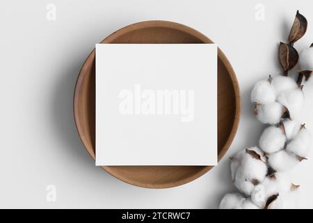 Einladungskarte Mockup auf einem Holzteller mit getrocknetem Baumwollzweig. Stockfoto