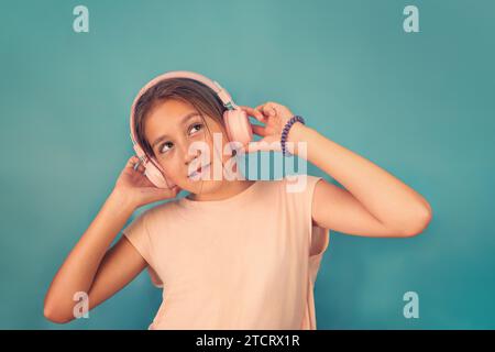 Glückliches lächelndes Kind hört Musik in Kopfhörern auf blauem Hintergrund. Lebhafte und lustige Emotionen, ein glückliches Kind mit Freude hört dem Lied zu Stockfoto