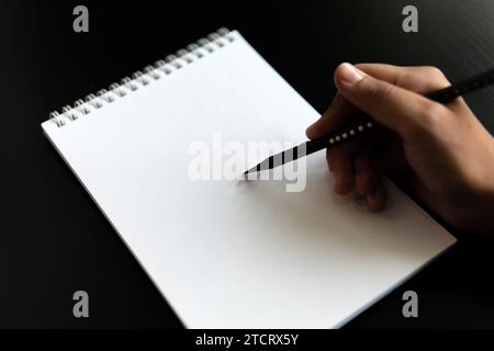 Eine Apfelstiftzeichnung in einem Notizbuch und ein Bleistift auf einem schwarzen Tisch. Lernen, ein Konzept zu zeichnen. Stockfoto