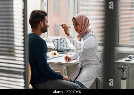 Junge Ärztin in Hijab bei der Untersuchung des Sehvermögens von Patienten Stockfoto