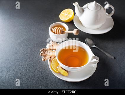 Tasse heißer Ingwertee mit frischer Ingwerwurzel und Zitrone auf grauem Hintergrund. Stockfoto