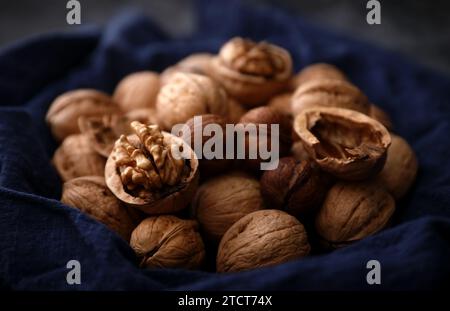 Eine Gruppe Walnüsse auf einem blauen alten Tuch am Fenster an einem dunklen Ort (außer Fokus, Makro) Stockfoto