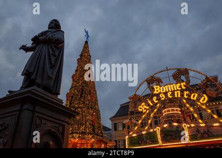 Bonn - 6. Dezember 2023 : Statue von Ludwig van Beethoven auf dem Weihnachtsmarkt mit festlichen Lichtern auf einem Riesenrad und Weihnachtsbaum im Hintergrund Stockfoto