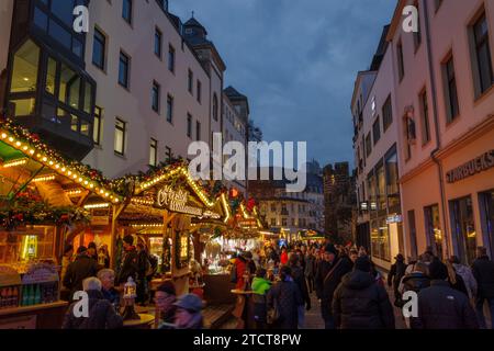 Bonn, Deutschland - 6. Dezember 2023: Dämmerlicher Blick auf den Weihnachtsmarkt mit festlichen Lichtern und Dekorationen, während die Käufer die Verkaufsstände nahe der alten Stadtmauer erkunden Stockfoto