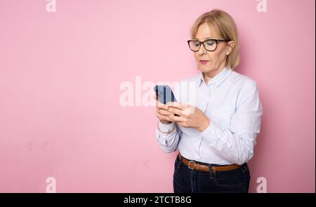 Glückliche ältere Frau, die ihr Smartphone mit mobilen Online-Apps in der Hand hält, lächelnd eine alte Dame mittleren Alters, die SMS-Nachrichten schickt, am Telefon chattet und sich ansieht Stockfoto