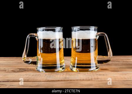 Zwei Glasbierkrüge mit Bier auf einem rauen Holztisch vor schwarzem Hintergrund. Kopierbereich. Stockfoto