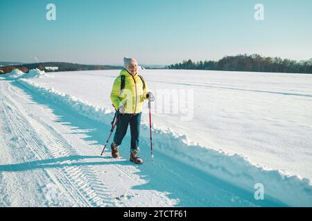Ältere Frau aus den 60er Jahren, die auf dem Hügel relaxt. Frau trinkt heißen Tee aus der Thermotasse und genießt den Panoramablick auf den Stadtpark. Stockfoto