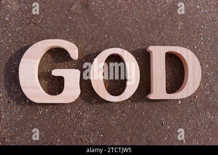 Hölzerne Buchstaben, die das Wort GOTT auf einem Hintergrund aus Strandsand bilden. Christliches Symbol. Stockfoto