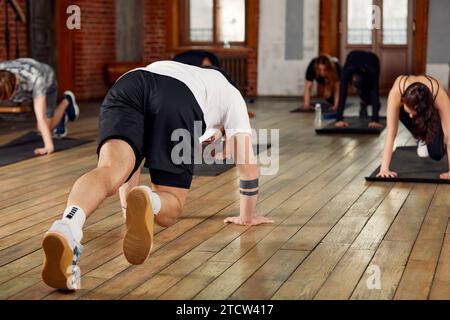Gruppe von sportlichen jungen Menschen in Sportbekleidung, die Liegestütze oder Planken im Fitnessstudio machen, Gruppenfitness-Konzept. Stockfoto