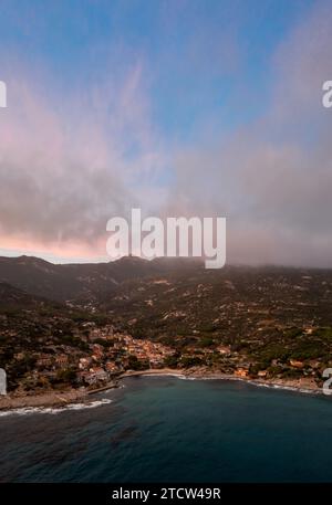 Ein Drohnenblick auf Seccheto Beach und das Dorf auf Elba Island kurz nach Sonnenuntergang mit einem nebligen lila Himmel Stockfoto