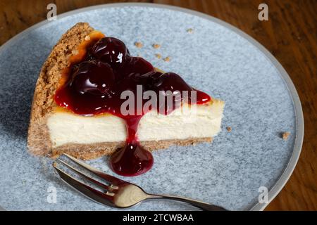 Eine in Scheiben geschnittene Portion eines tiefgefüllten New Yorker Käsekuchens mit schwarzen Kirschen. Der Kuchen wird auf Teller serviert. Stockfoto