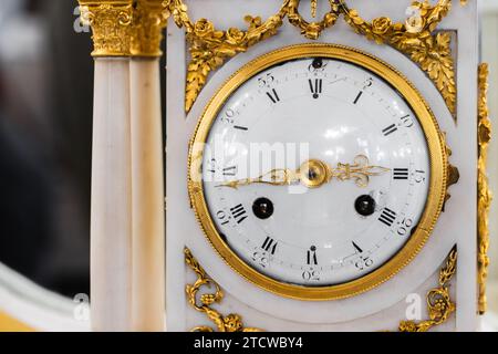 Vintage-Kaminuhr, Nahaufnahme, Vorderansicht. Uhr aus weißem Emaille mit römischen Ziffern und goldenen Zeigern, Zeitmesser im Barockstil Stockfoto