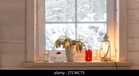 Weihnachtslaterne, Weihnachtskaktus, Geschenk, Kerzen am Fenster des Holzhauses, Wintergarten Stockfoto