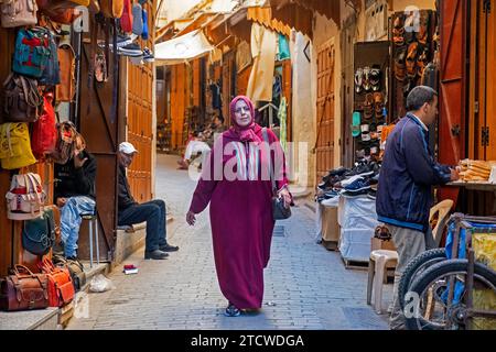 Marokkanische muslimische Frau trägt Djellaba / Jillaba und Hijab in einer Gasse mit Geschäften in der Medina der Stadt Fes / Fès, Fès-Meknes, Marokko Stockfoto