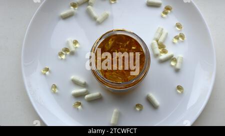 Glas mit goldenen Fischöl Kapseln mit Vitaminen E und gesunden Fetten von oben auf einer großen weißen Platte mit anderen Kapseln verstreut, nehmen Omega 3 Diät Stockfoto
