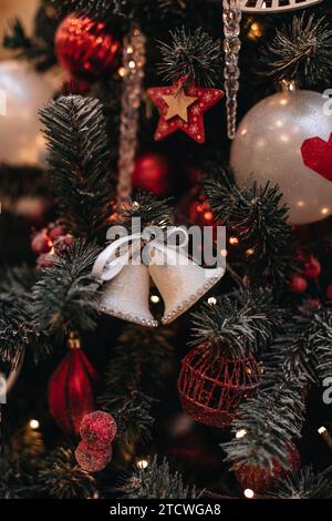 Weiße Zauberglocken mit Band, die an einem Weihnachtsbaum hängen, mit zauberhaften Lichtern. Dekorierte Fichtenzweige. Stockfoto