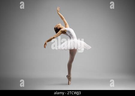 Aufnahme einer Ballerina in voller Länge, die auf grauem Hintergrund tanzt und sich nach hinten lehnt Stockfoto