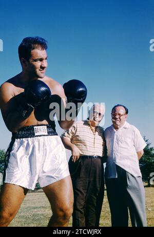 FERNDALE, NY – 8. AUGUST: Der US-amerikanische Boxer Rocky Marciano (1923–1969) posiert für ein Porträt, während sein Manager Al Weill und Trainer Charlie Goldman am 8. August 1955 in Ferndale, New York, im Grossinger's Resort anschauen. (Foto von Hy Peskin) *** örtlicher Bildtitel *** Rocky Marciano;Al Weill;Charlie Goldman Stockfoto