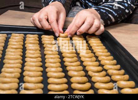 Nahaufnahme von nussigen Süßigkeiten, in Reihen auf schwarzem Backblech gestapelten Vanillerollen. Weibliche Hände mit rohen sichelförmigen Nusskeksen der tschechischen Weihnachtsküche. Stockfoto