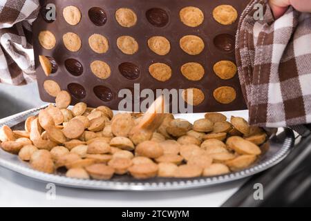 Nahaufnahme frischer Kekse in halbierter Walnussform beim Herabfallen aus brauner Silikon-Backform. Haufen Nusssüße auf silberner Platte. Tschechisches Weihnachtsgebäck. Stockfoto
