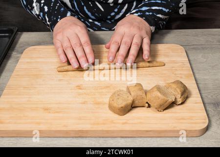 Nahaufnahme menschlicher Hände, die mit rohem nussigem Shortbread-Teig auf Holzrollbrett arbeiten. Zubereitung von leckeren süßen Keksen Vanillebrötchen. Tschechische Küche. Stockfoto
