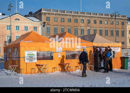 An einem sonnigen Wintertag in Helsinki, Finnland, stehen die Leute für das Orangenzelt-Café auf dem schneebedeckten Marktplatz an Stockfoto