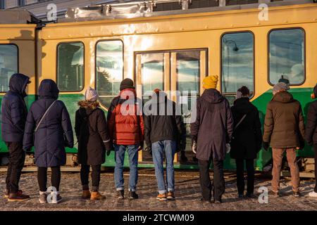 Menschen in Winterkleidung, die auf dem Bürgersteig stehen und auf die Straßenbahnfahrt in Helsinki, Finnland, warten Stockfoto