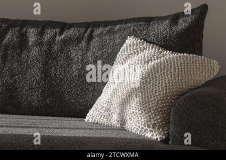 Weißes, strukturiertes Dekokissen auf einem dunkelgrauen Sofa. Wabi-sabi Innenausstattung zur Dekoration Stockfoto