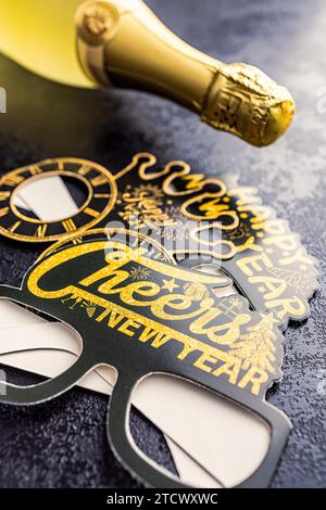 Happy New Year Hintergrund. Schwarze, lustige Papiergläser und eine Flasche Champagner auf dem schwarzen Tisch. Stockfoto