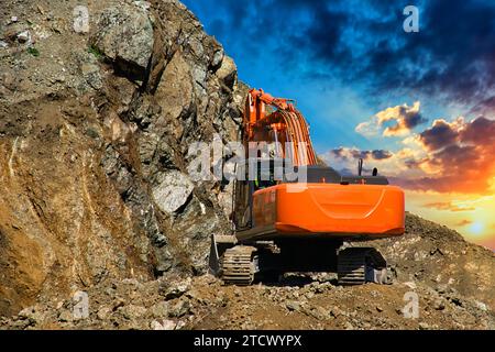 Bagger auf einer Baustelle an der Seite eines Hügels vor einem bewölkten blauen Himmel. Kompakte Baumaschinen für Erdbewegungsarbeiten. Ein unverzichtbares Produkt Stockfoto