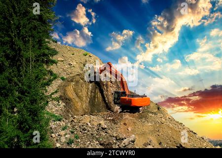 Bagger auf einer Baustelle an der Seite eines Hügels vor einem bewölkten blauen Himmel. Kompakte Baumaschinen für Erdbewegungsarbeiten. Ein unverzichtbares Produkt Stockfoto