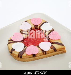 Herzförmiger Keks mit Erdbeermarmelade isoliert auf weißem Hintergrund. Traditionelle Linzer Kekse auf dem Teller Nahaufnahme. Stockfoto