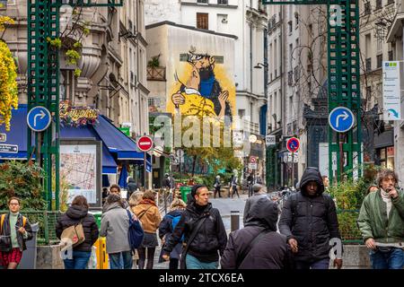 Leute laufen entlang der Rue Montorgueil, mit einem Street Art Gemälde von Tintin und Captain Haddock, die sich im Hintergrund auf einem Gebäude in Paris, Frankreich, küssen Stockfoto