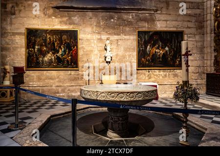 Eine ruhige Taufkammer in der Kathedrale von Sevilla mit einem Marmorbecken, religiösen Gemälden und einer eleganten Kerze, die die heilige Atmosphäre einfangen. Stockfoto