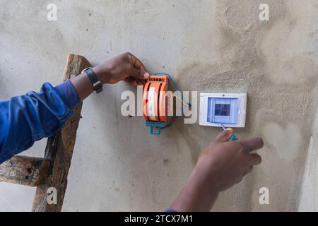 Vordergrundaufnahme der Hände eines Elektrikers auf einer Leiter, die eine Kiste an der Wand öffnet. Stockfoto