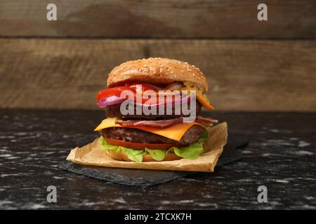 Köstlicher Burger mit Fleischkoteletts, Speck, Käse, Gemüse und Salat auf schwarzem Tisch Stockfoto