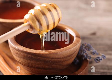 Leckerer Honig aus dem Pendelarm in eine Schüssel auf Holztisch gießen, Nahaufnahme Stockfoto