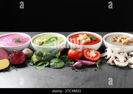 Verschiedene leckere Cremesuppen in Schüsseln und Zutaten auf dunkelgrauem Tisch Stockfoto