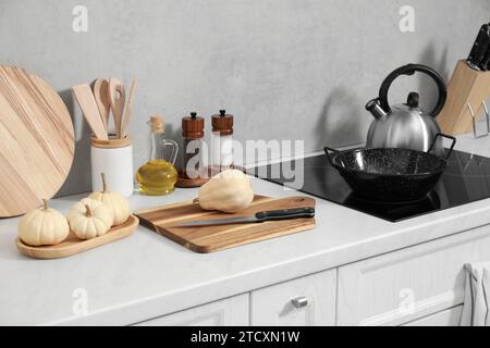 Schneidebretter aus Holz, andere Kochutensilien und Kürbisse auf weißer Arbeitsplatte in der Küche Stockfoto