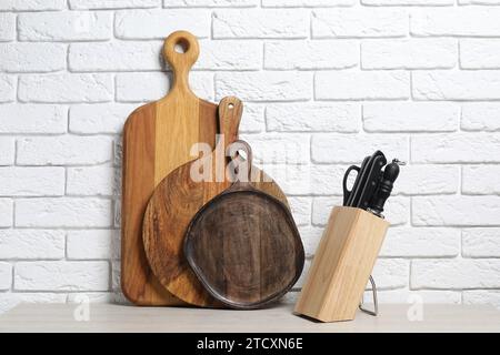 Verschiedene Schneidebretter und Messer aus Holz im Halter auf dem Leuchttisch in der Nähe der weißen Ziegelwand Stockfoto