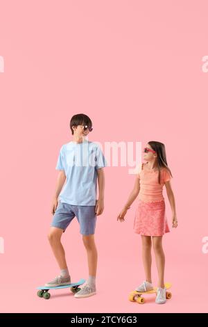 Niedliches Mädchen und ihr Bruder mit Skateboards auf rosa Hintergrund Stockfoto
