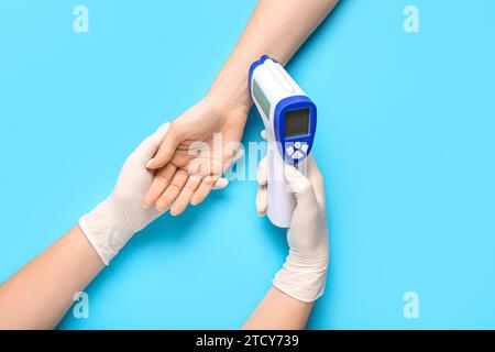 Arzt mit Infrarot-Thermometer zur Temperaturmessung des Patienten auf blauem Hintergrund Stockfoto